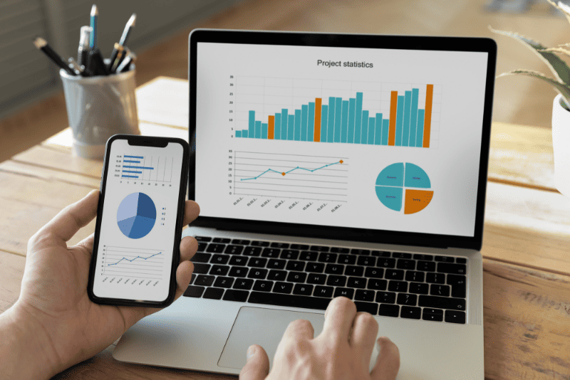 プロジェクトの統計データが表示されたノートパソコンとスマートフォンを使う様子